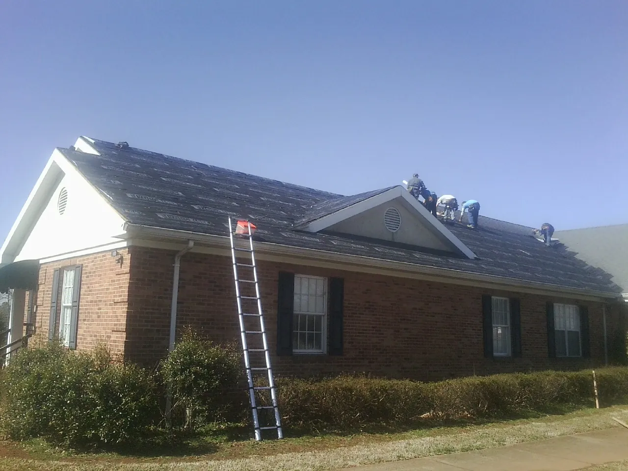 Crew tearing shingles off a brick ranch roof with a ladder set — Emergency Roof Repair work by our crew in Saint Inigoes