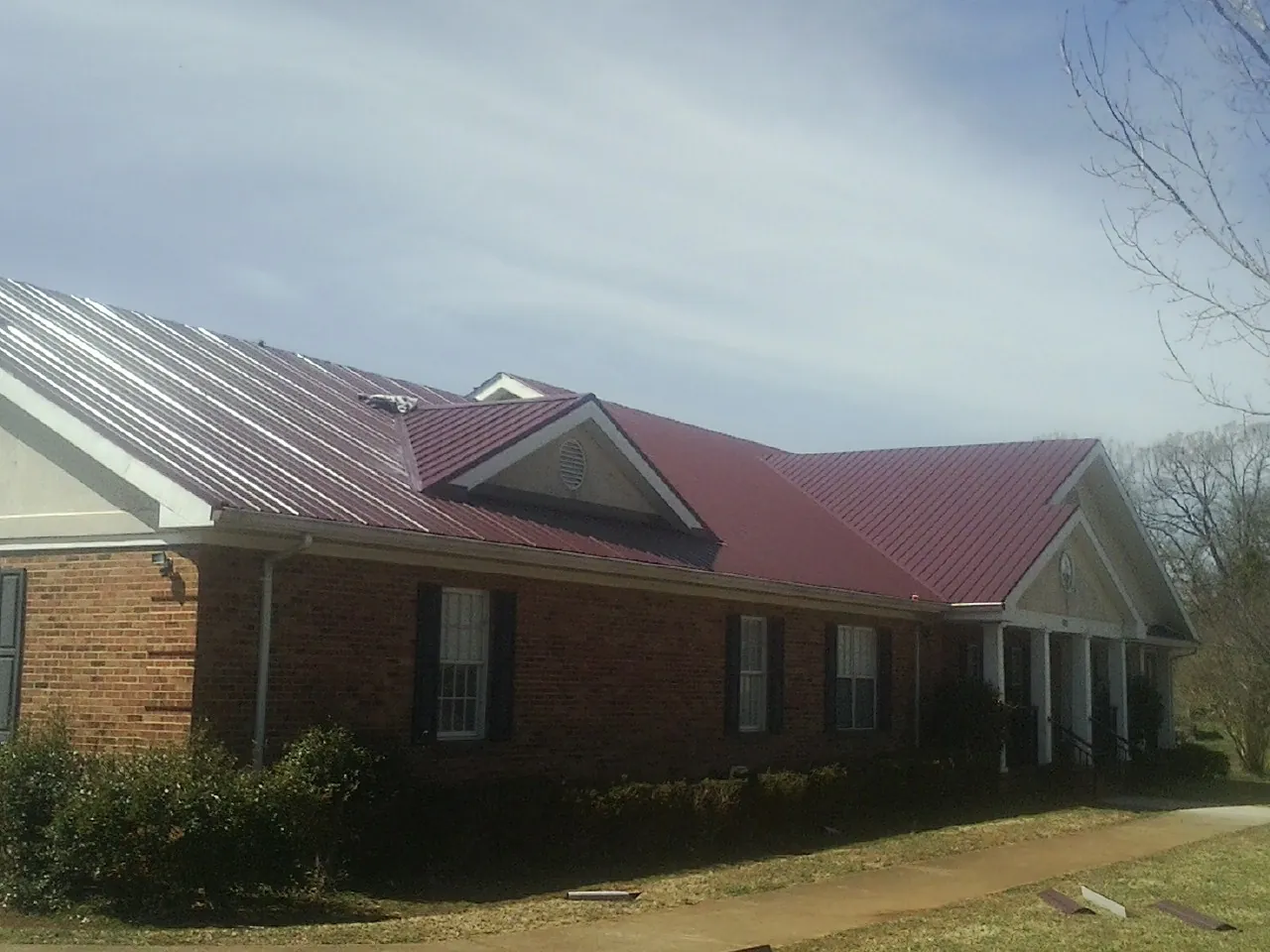Red metal roof with gabled entries on a long brick building, from a Hail Damage Roof Repair job in Saint Inigoes