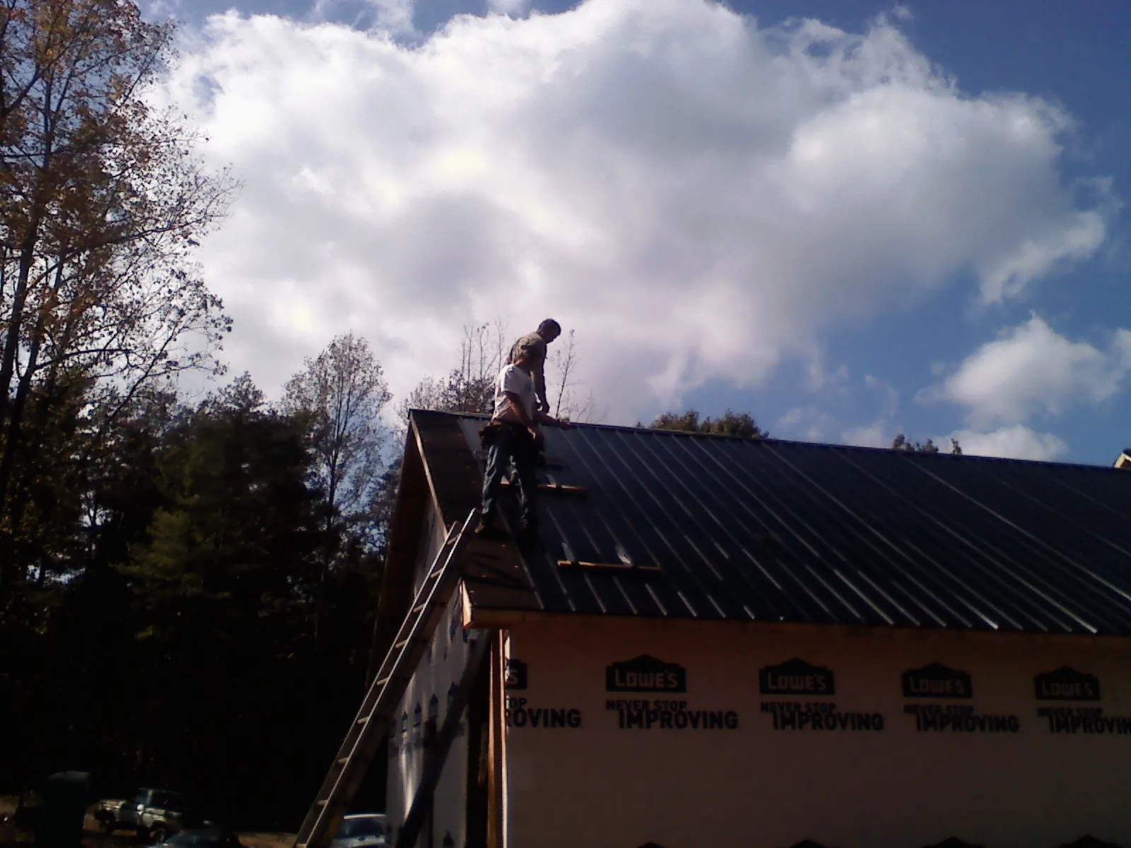 Roofer fastening dark metal panels high against a cloudy sky, from a Roof Inspection job in Saint Inigoes