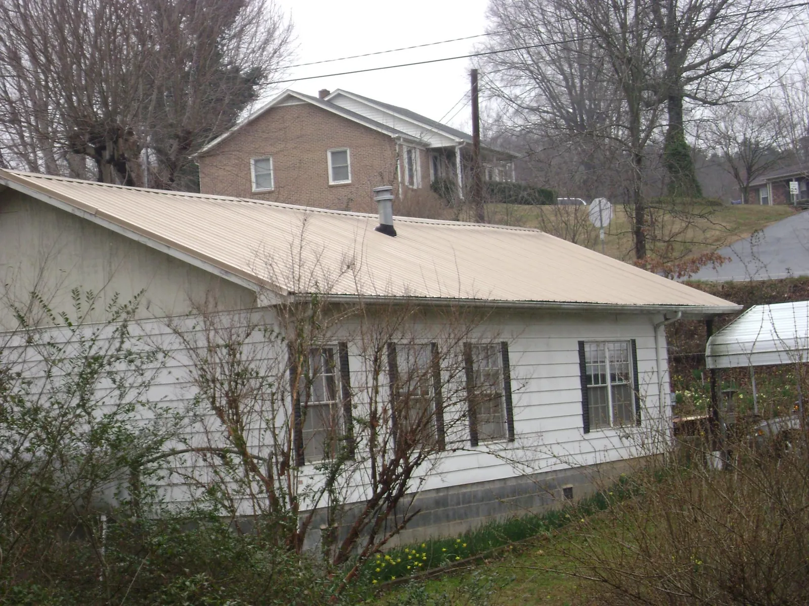 Tan metal roof on a white sided house set into a hillside — Commercial Roofing by Roofing Brothers in Saint Inigoes
